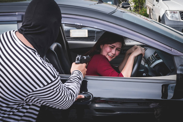 強盗は彼女の車を強奪しようし、若い女性を怖がらせるために銃を指して. - 写真・画像