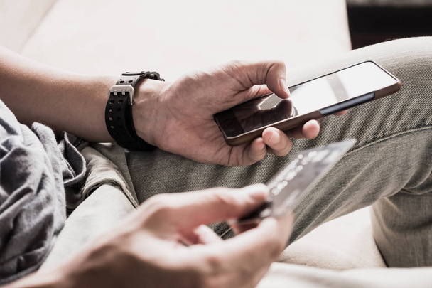 Κοντινό πλάνο της αρσενικό χέρια χρησιμοποιώντας smartphone και η κατοχή πιστωτικής κάρτας. Online αγορές έννοια. επιλεκτική εστίαση - Φωτογραφία, εικόνα
