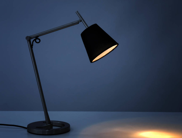Stylish desk lamp on table in darkness - Valokuva, kuva