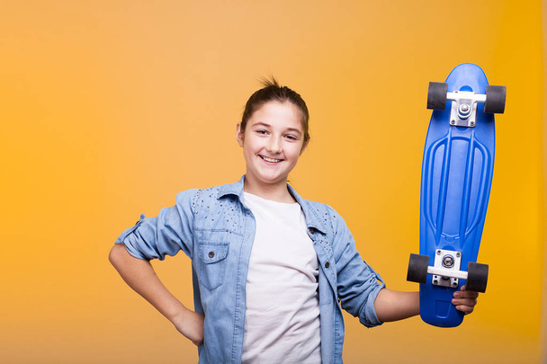 Smiling teenager girl looking at camera and holding a blue skate - Φωτογραφία, εικόνα