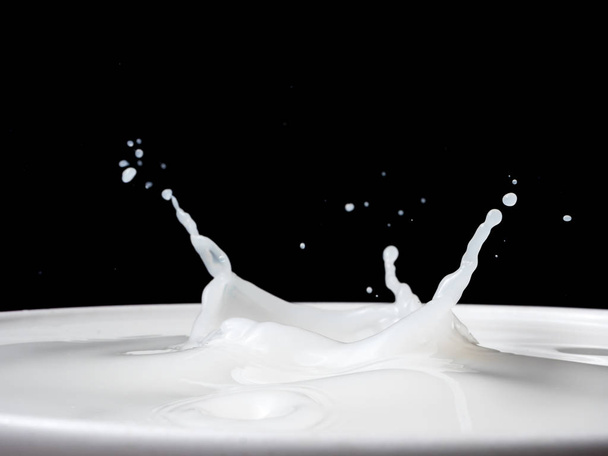 Spritzer Milch aus einer Tasse auf schwarzem Hintergrund. - Foto, Bild