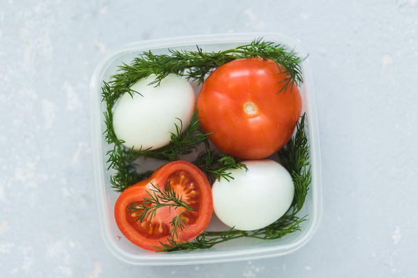 Ripe tomatoes and eggs in container on grey background close up. Healthy diet. - 写真・画像