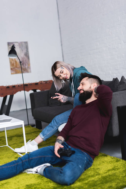 tattooed couple playing video game in living room - Photo, image