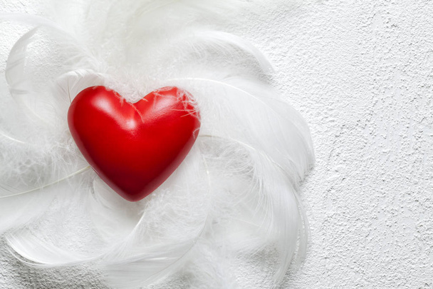 Red heart and white feathers on plastered background - Zdjęcie, obraz