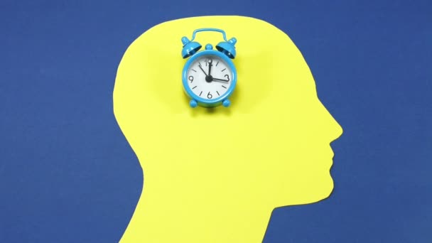 Pequeño reloj despertador de timbre, corriendo y colocado en un contorno de cabeza masculino amarillo, sobre un fondo azul, imágenes conceptuales
 - Imágenes, Vídeo