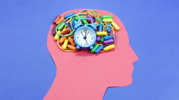 Verstrikt elastiekjes, gekleurde pillen en kleine bell ring wekker, uitgevoerd en geplaatst op een rode mannelijke hoofd contour, tegen een blauwe achtergrond, conceptuele beelden - Video