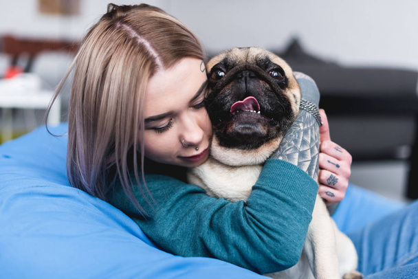 beautiful tattooed girl hugging funny pug at home - Foto, immagini