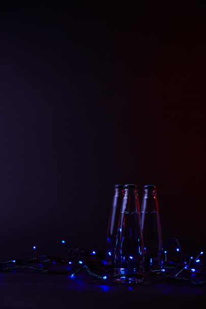 trzech zamkniętych butelkach wody z niebieski garland na ciemnej powierzchni - Zdjęcie, obraz