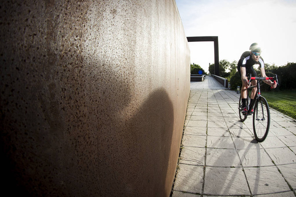 Велосипедист едет возле металлической стены и травы
 - Фото, изображение