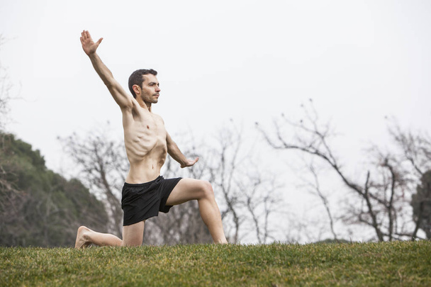 man performing abdominal exercise with one knee on the grass - Photo, Image