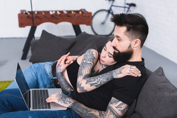 Widok z boku z tatuażem para patrząc na laptopa w domu - Zdjęcie, obraz