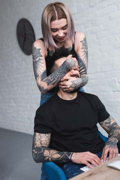 tattooed girlfriend covered boyfriends eyes while he working at computer - Foto, afbeelding
