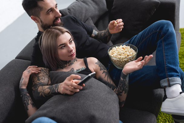tattooed couple watching tv on sofa at home - 写真・画像
