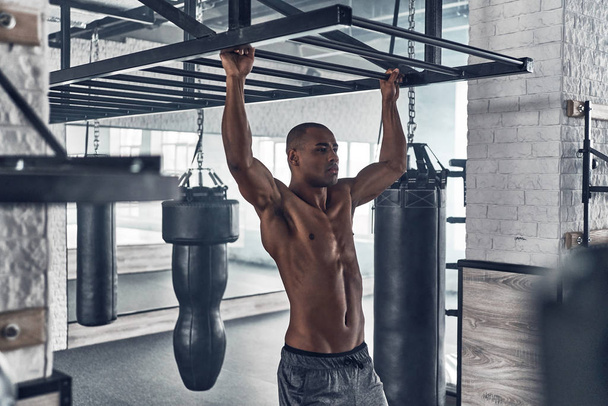Shirtless muscular mixed race man doing pull ups in gym - Fotografie, Obrázek
