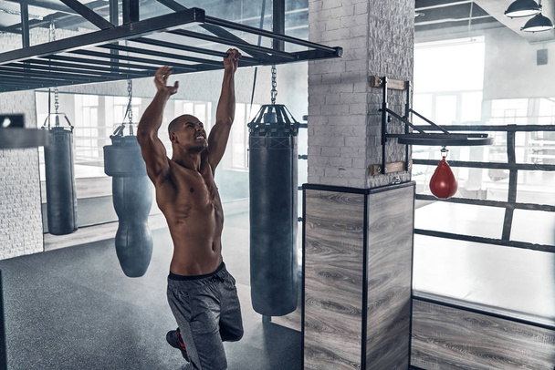 shirtless strong muscular man hanging on pull up bar in gym - Foto, Bild