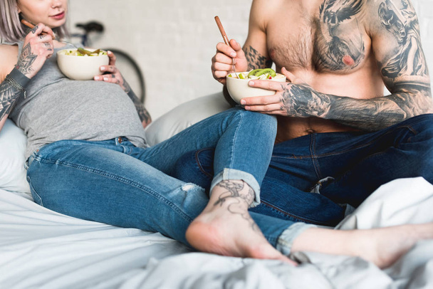cropped image of pregnant tattooed girlfriend eating salad with boyfriend at home - Foto, afbeelding