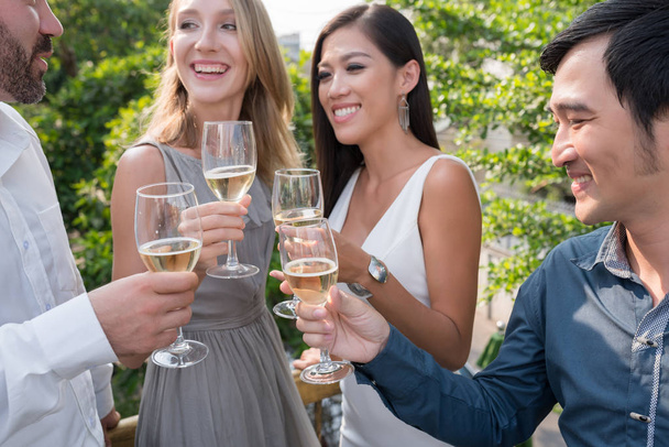 fröhliche junge Leute in schönen Kleidern genießen Weißwein und plaudern miteinander - Foto, Bild