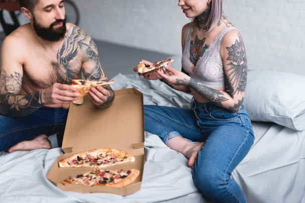 abgeschnittenes Bild von tätowiertem Paar, das zu Hause Pizza isst - Foto, Bild