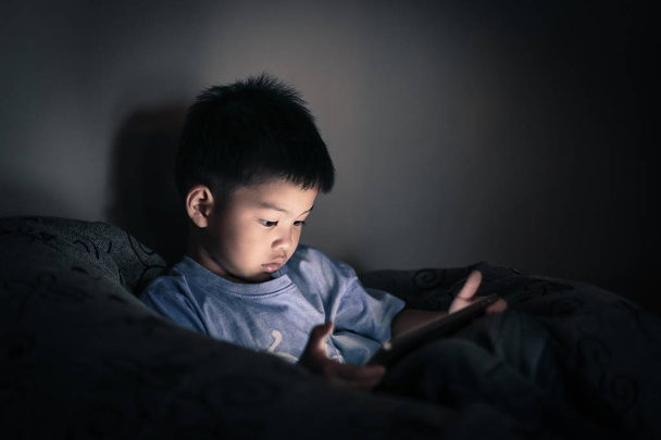 Αγόρι βλέποντας tablet στο σκοτάδι σαλόνι. - Φωτογραφία, εικόνα