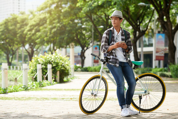 Stílusos ázsiai ember hajlik a kerékpáros smartphone - Fotó, kép