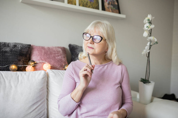 Senior lady in glasses holding ball pen thinking - Фото, изображение