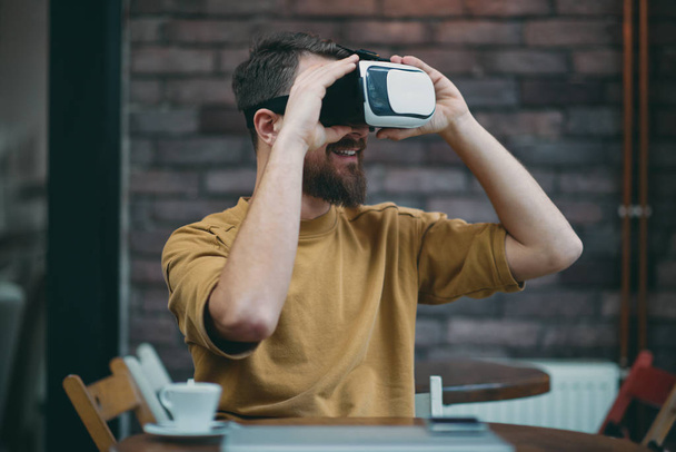 Hombre joven usando caja de realidad virtual mientras está sentado en la cafetería
. - Foto, imagen
