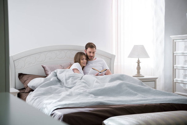 Couple lying and reading book in modern bedroom - Photo, image