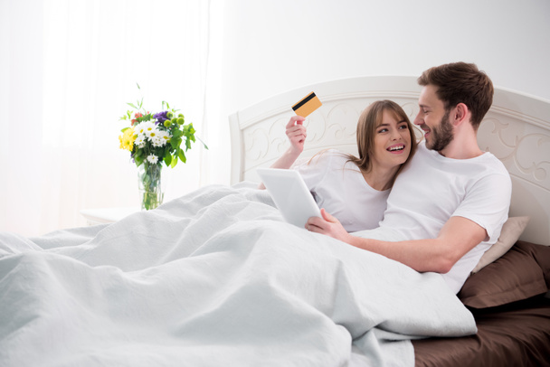 Couple doing online shopping while lying in cozy modern bedroom - Zdjęcie, obraz