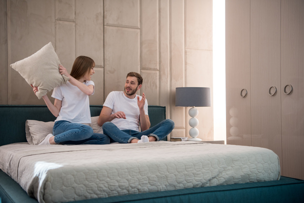 Woman going to hit her boyfriend by pillow in cozy bedroom - Fotografie, Obrázek