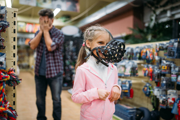 family choosing muzzle for domestic animal in pet shop, father and little daughter having fun in petshop - Φωτογραφία, εικόνα