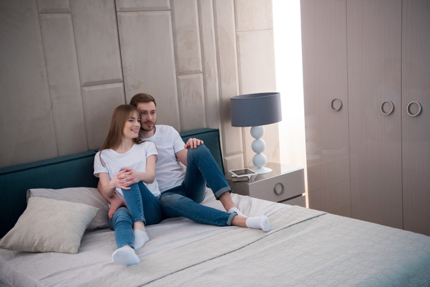 Jovem casal sentado na cama com travesseiros no quarto moderno
 - Foto, Imagem