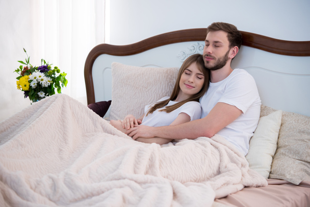 Fiatal pár, átölelve az ágyban, csukott szemmel, modern hálószoba - Fotó, kép