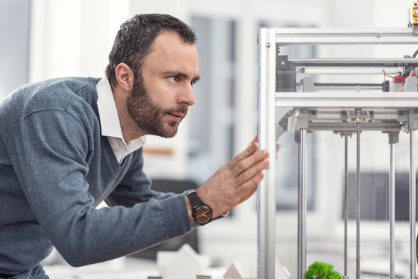 Serious young engineer repositioning 3D printer - 写真・画像