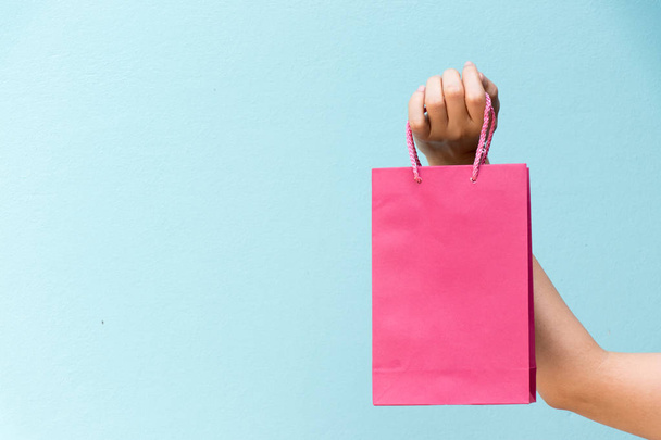 Hand of business woman hold pink shopping bag on blue concrete background - Photo, Image