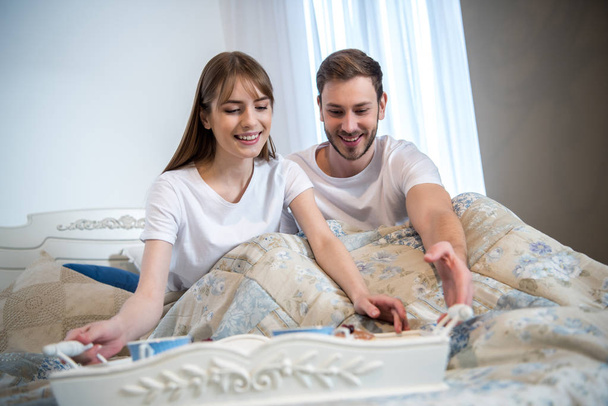 Echtpaar in bed met ontbijt op dienblad in moderne slaapkamer - Foto, afbeelding