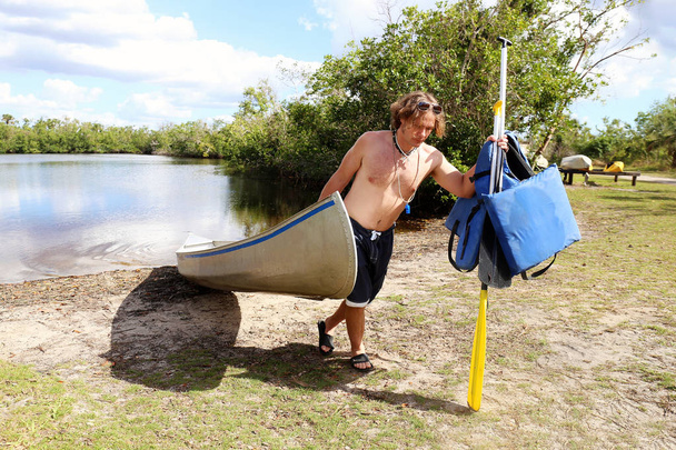El hombre que lleva la vieja canoa fuera del río en los Everglades
 - Foto, imagen