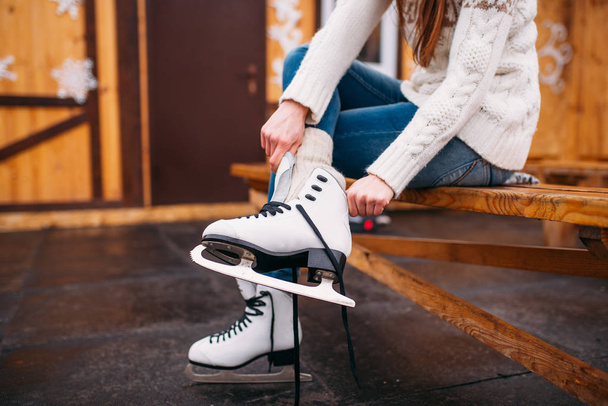 Nuori nainen istuu jäällä ja sitominen kengännauhat luistimet, luistinrata
 - Valokuva, kuva