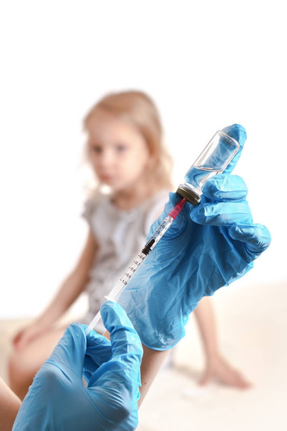 Vaccination concept. Doctor holding a syringe with a liquid inside next to a girl arm. Blurred background of a girl. - Photo, Image