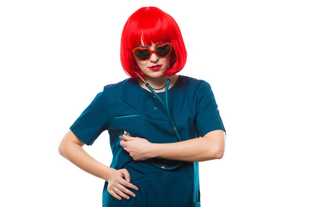 Молодая женщина-врач в красном парике проверяет сердцебиение
  - Фото, изображение