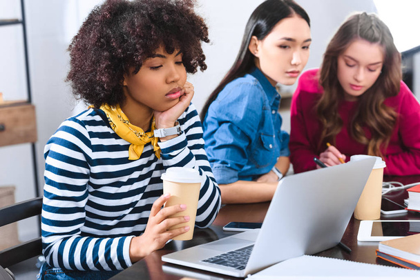 selective focus of bored african american young woman with laptop and multicultural students near by - 写真・画像