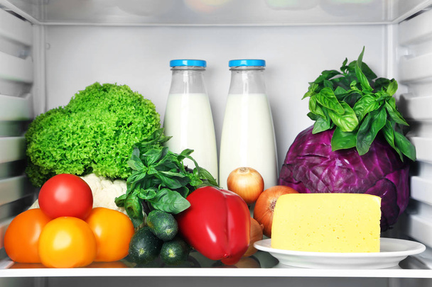 Nevera abierta llena de verduras con queso y botella de leche
 - Foto, Imagen