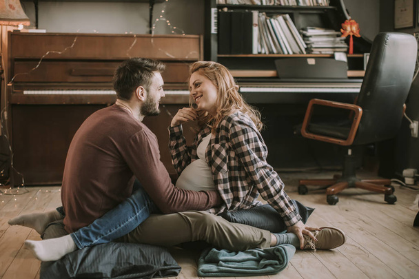 Young man and pregnant woman sitting on the floor in the room - Photo, Image