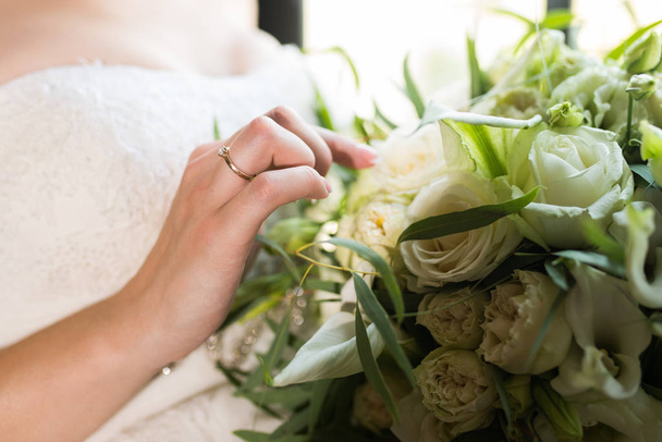 Braut berührt Braut Brautstrauß mit einer Hand mit Ehering am Finger. Details zur Hochzeit - Foto, Bild