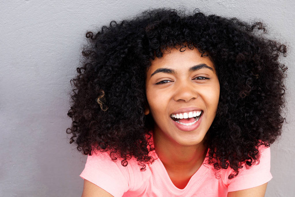 Primer plano retrato de la atractiva joven afroamericana riendo contra la pared gris
 - Foto, imagen