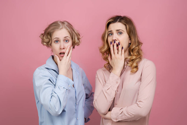 young attractive girls shocked and very surprised. Their eyes are wide open and their mouths open. Fear in their eyes is caused by a terrible incident. Studio portrait on pink background - Photo, image
