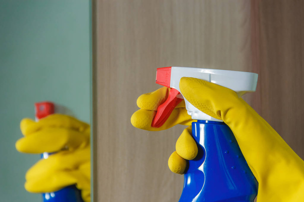 Female Hand in Yellow Glove Cleaning Mirror with Spray Cleaner. in Blue Bottle, Housework, Spring Cleaning Concept. - Foto, imagen