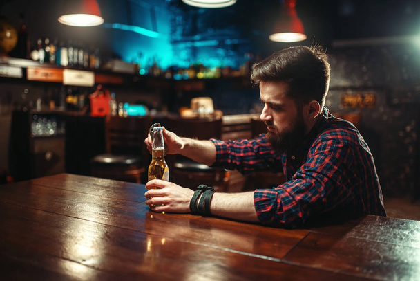 Junger Mann öffnet Flasche Bier an Theke, Alkoholismus, Trunkenheitskonzept - Foto, Bild