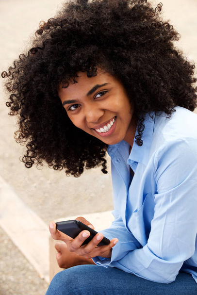 Close up portrait of beautiful young black girl sitting outside with mobile phone - Foto, Bild