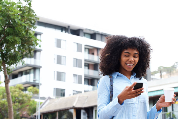 都市の外で携帯電話と歩いているアフリカ系アメリカ人の少女の肖像画 - 写真・画像