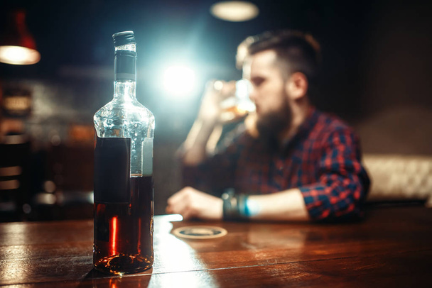 young man with bottle of whiskey at bar counter, alcoholism,  drunkenness concept - Photo, Image